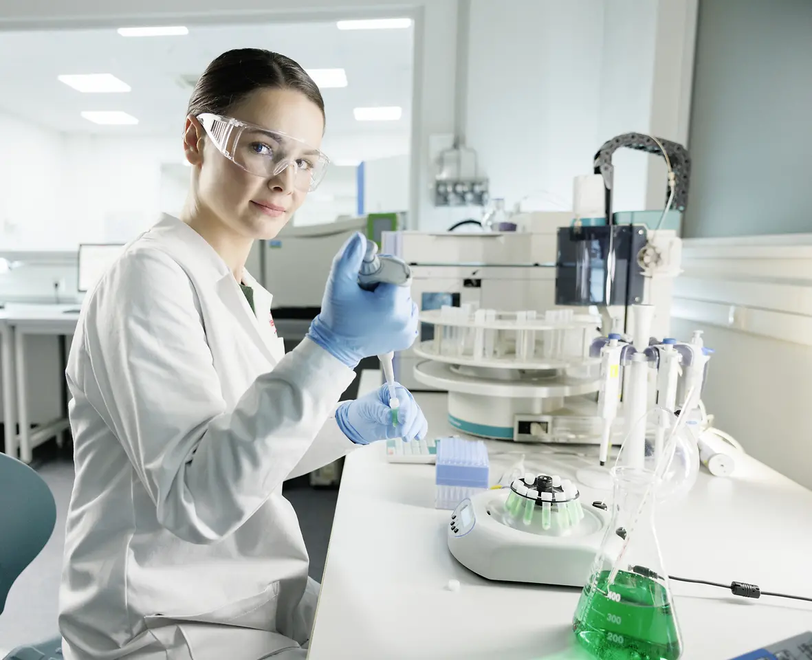 Bir bilim insanı laboratuvarda deney yapıyor, laboratuvar önlüğü ve koruyucu gözlük takıyor.