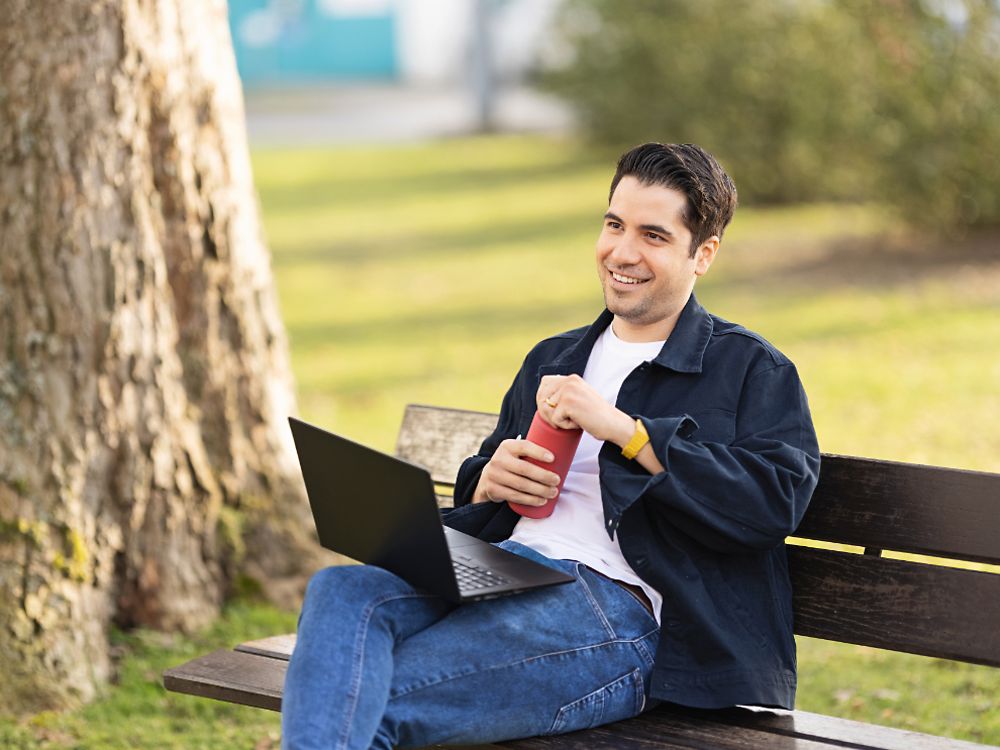Bir Henkel çalışanı, parkta bir bankta oturuyor ve dizüstü bilgisayarında çalışıyor. 