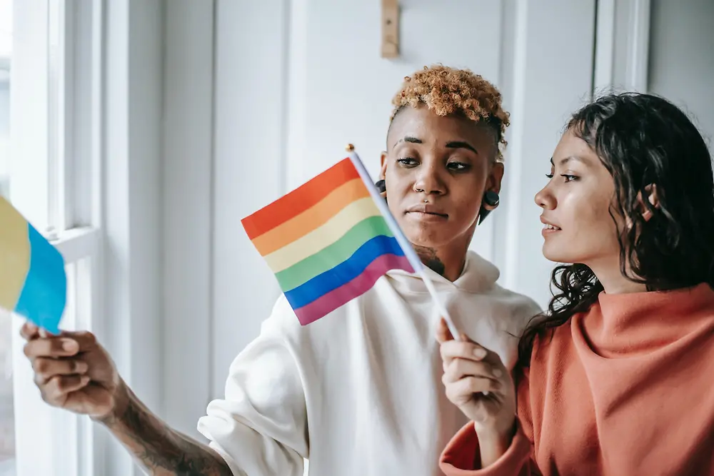 İki kadın, ellerinde LGBTQ+ bayraklarını tutarak konuşuyorlar.